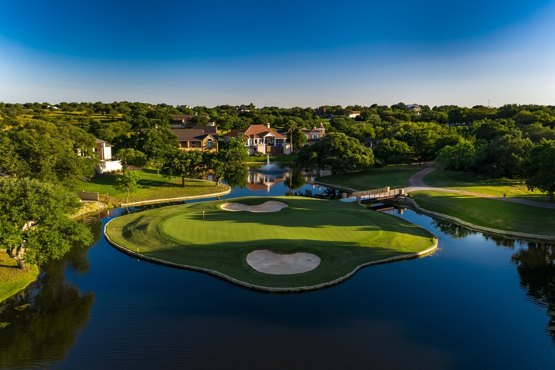 A golf green completely surrounded by water with homes in the background.